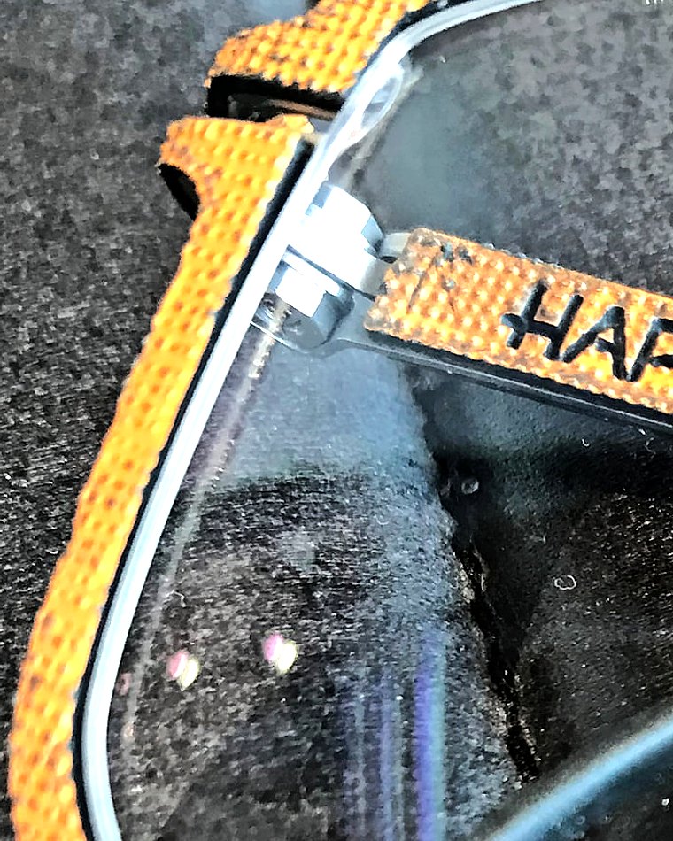 Macro detail of a Hapter frame — the hand-woven orange textile temple and metal hinge, hand made in Italy.