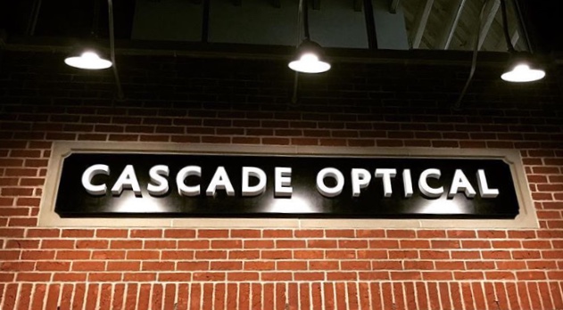 The illuminated CASCADE OPTICAL sign on the brick storefront at dusk.